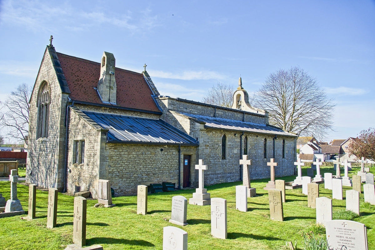 Stone church with a cemetery featuring gravestones under a clear blue sky.