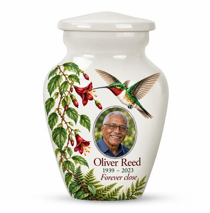 One white hummingbird keepsake urn with red hanging flowers and green fern leaves and Oliver Reed sample photo and text