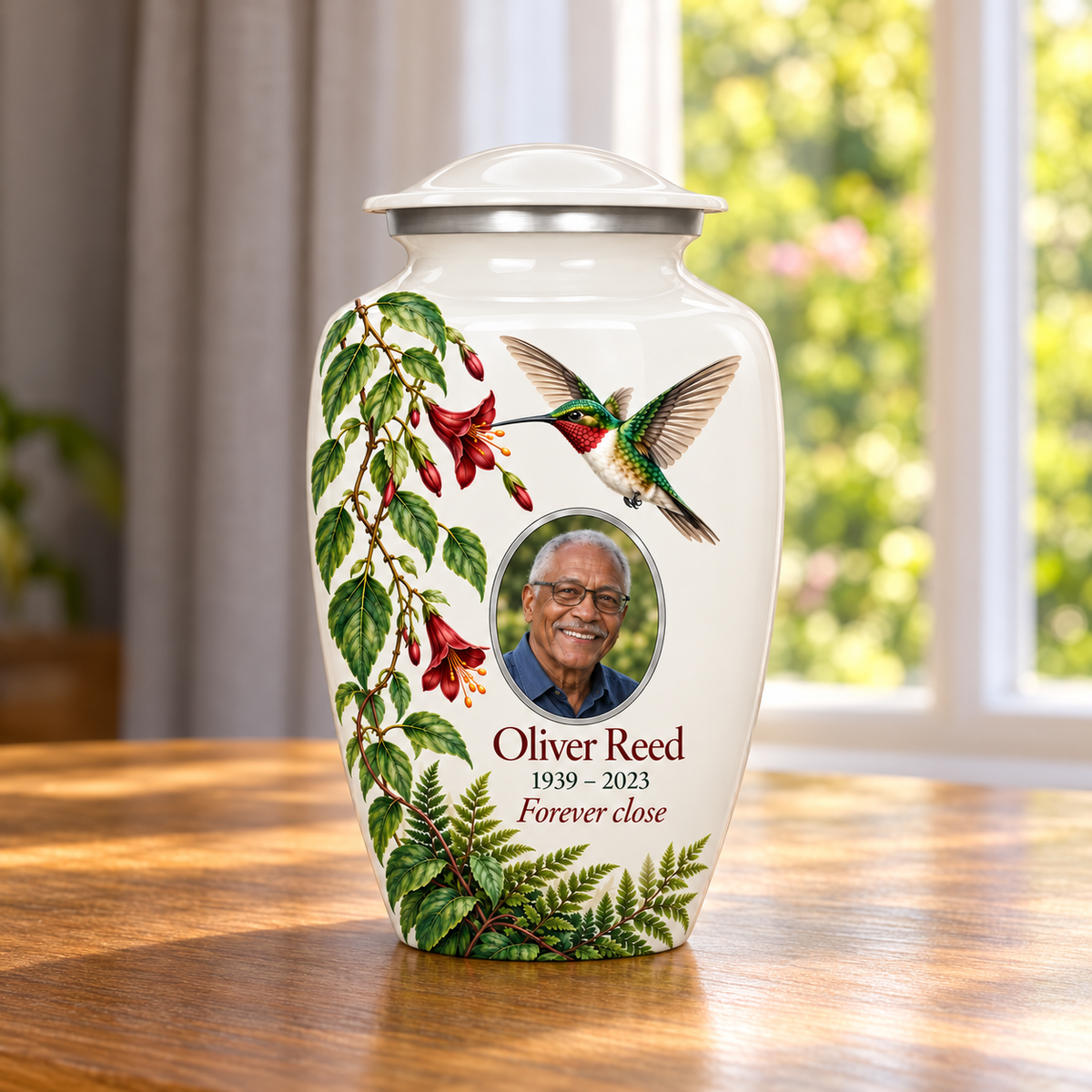 White hummingbird adult urn with red hanging flowers and green fern leaves and Oliver Reed sample photo and text in a sunlit home