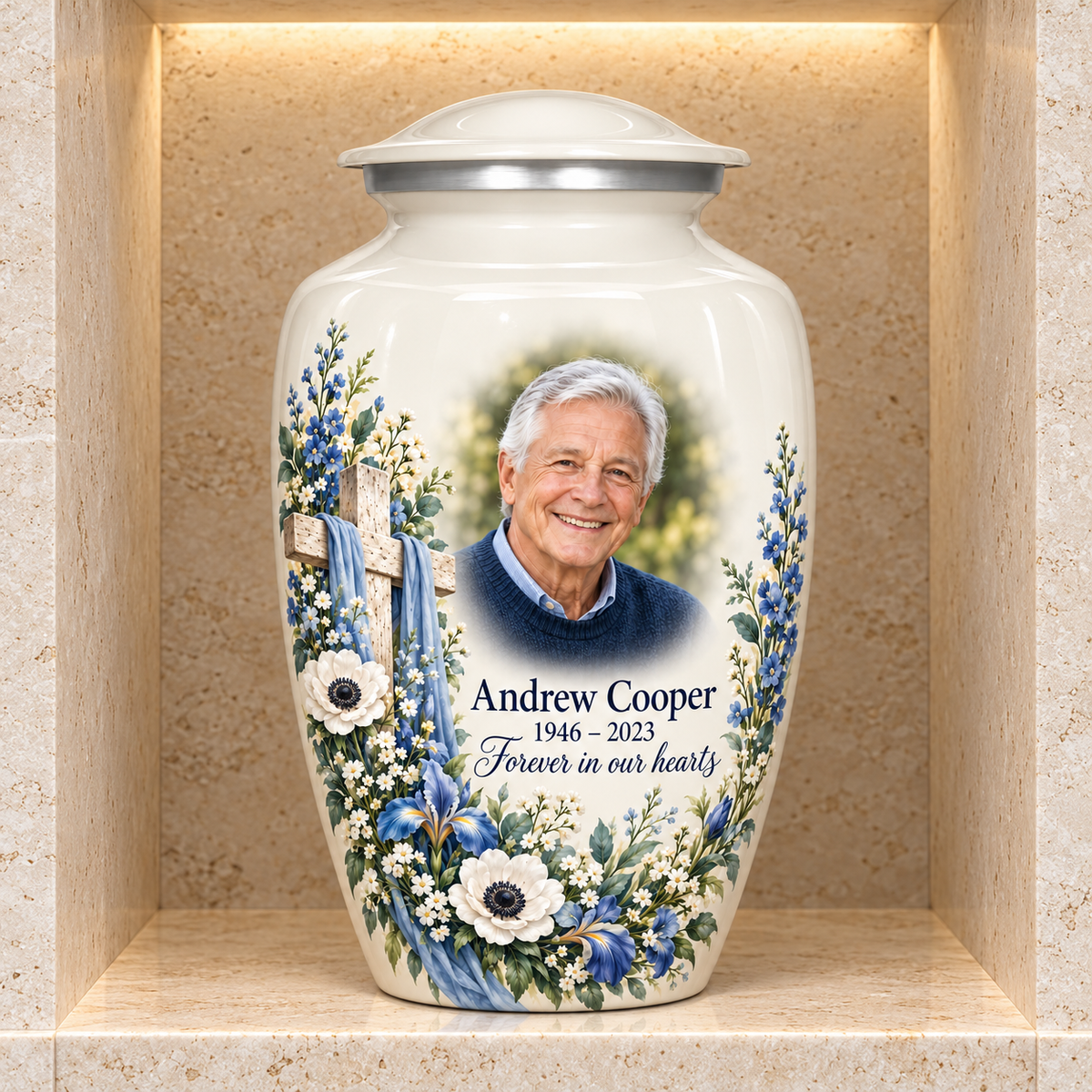 White adult cross urn with blue and white flowers displayed in a stone columbarium niche.