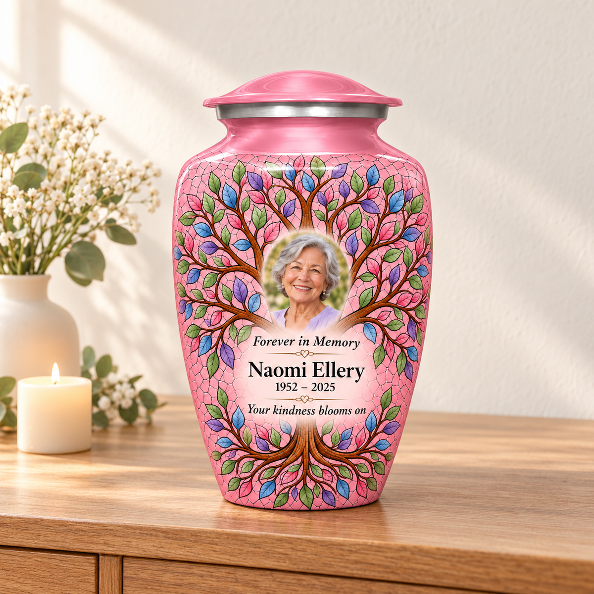 Pink Tree of Life adult urn with Naomi Ellery sample portrait on a wooden console beside a cream candle and white flowers.