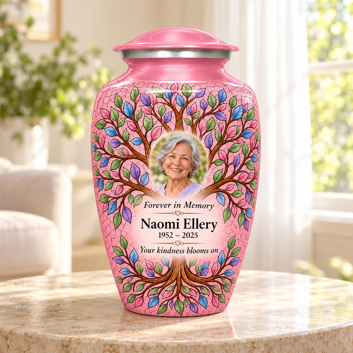 Pink Tree of Life adult urn with Naomi Ellery sample portrait and memorial text on a round stone table beside a sunlit window.