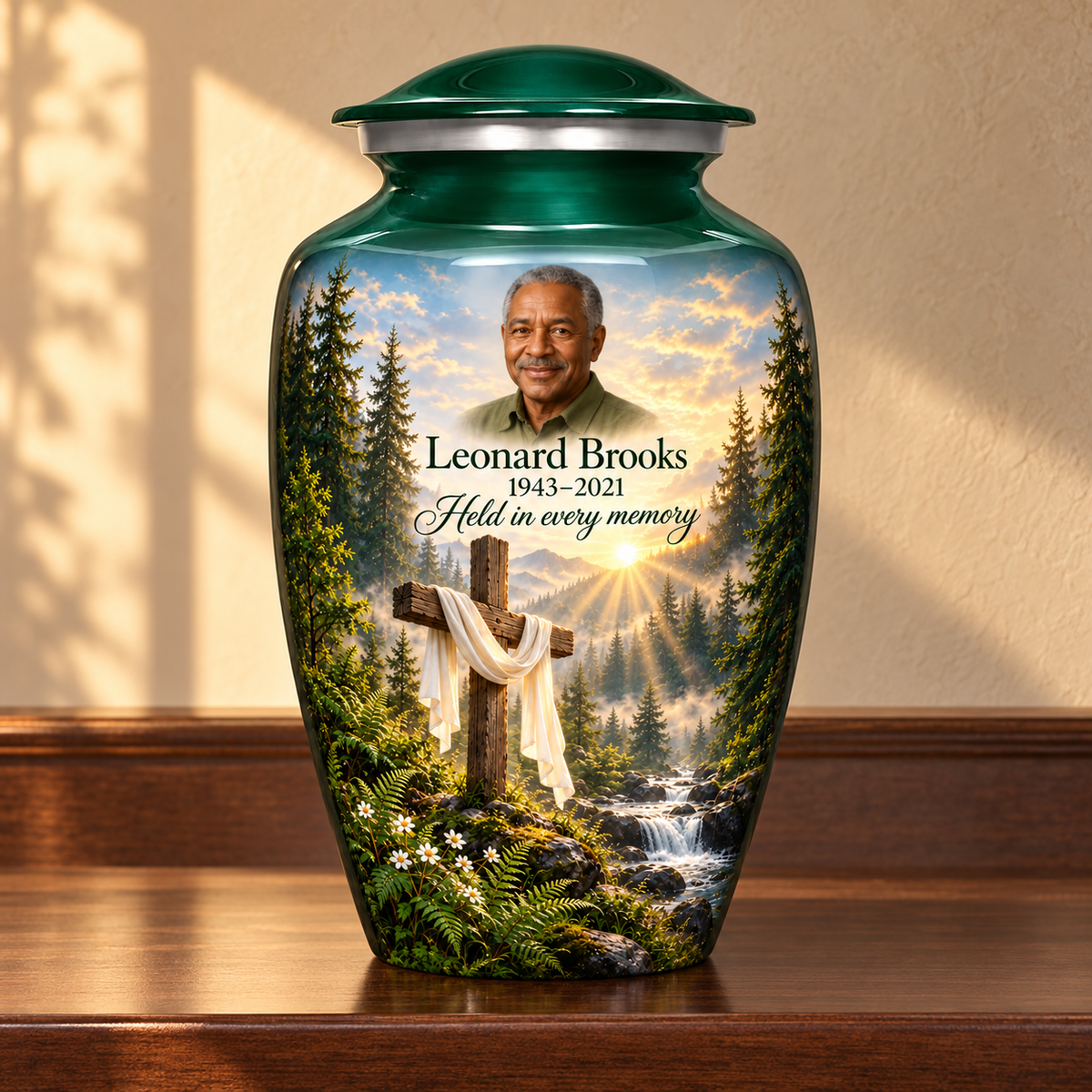 Green adult cross urn with a sunlit woodland stream displayed on a memorial console.