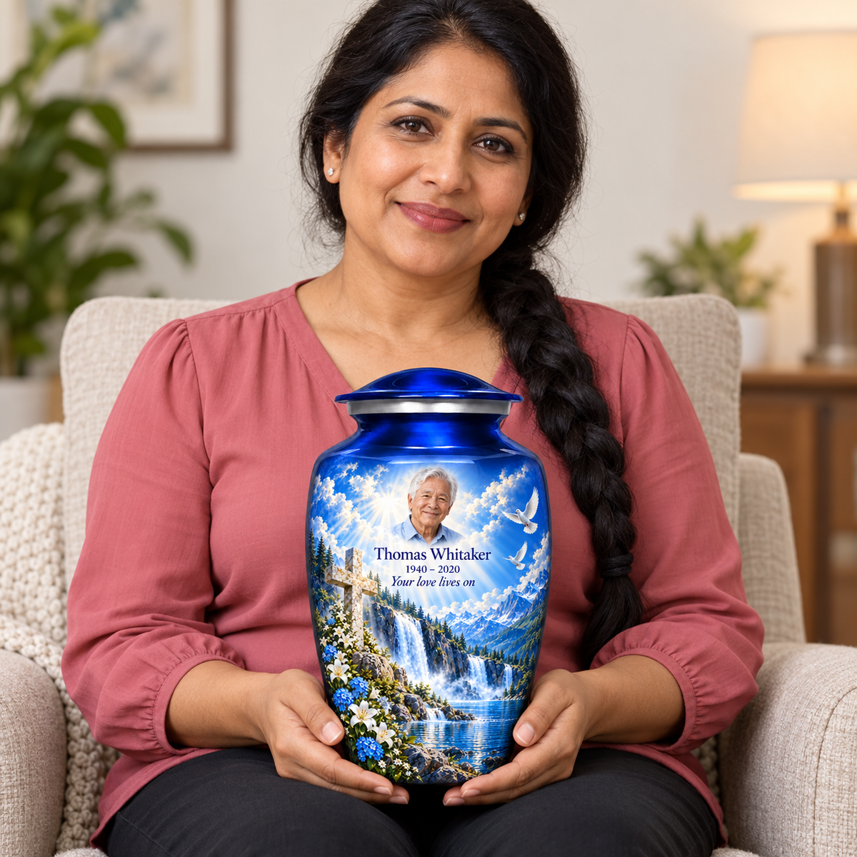 A seated person holding the blue cross urn with blue waterfalls and white flowers on their lap.