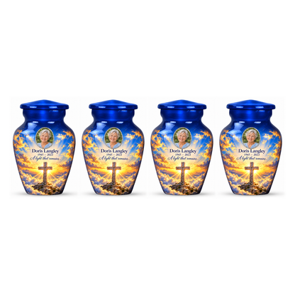 Four matching blue cross keepsake urns with golden sunlight and clouds arranged on white.