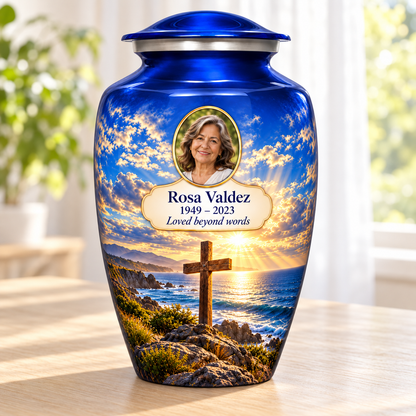 Blue adult cross urn with a blue coastal sunset beside a sunlit window.
