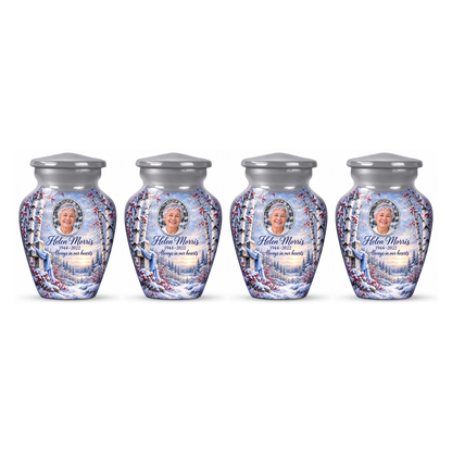 Four matching silver cross keepsake urns with snowy birches and red berries arranged on white.