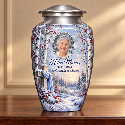 Silver adult cross urn with snowy birches and red berries displayed on a memorial console.