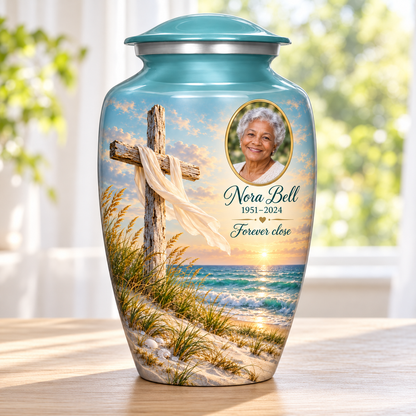 Green adult cross urn with sandy dunes and sea beside a sunlit window.