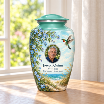 Seafoam green hummingbird adult urn with Joseph Quinn sample portrait and memorial text on a wooden table beside a sunlit window.