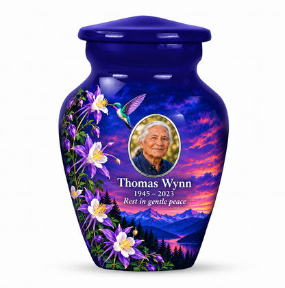 One indigo blue hummingbird keepsake urn with purple and white columbines and twilight mountains, Thomas Wynn sample portrait and memorial text on white.