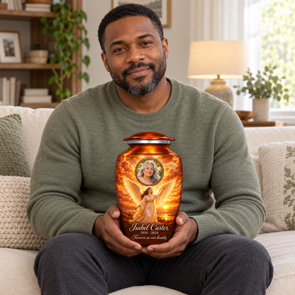 A seated person holding the orange angel urn with a standing angel over sunset water and a bronze colored oval sample portrait frame on their lap.