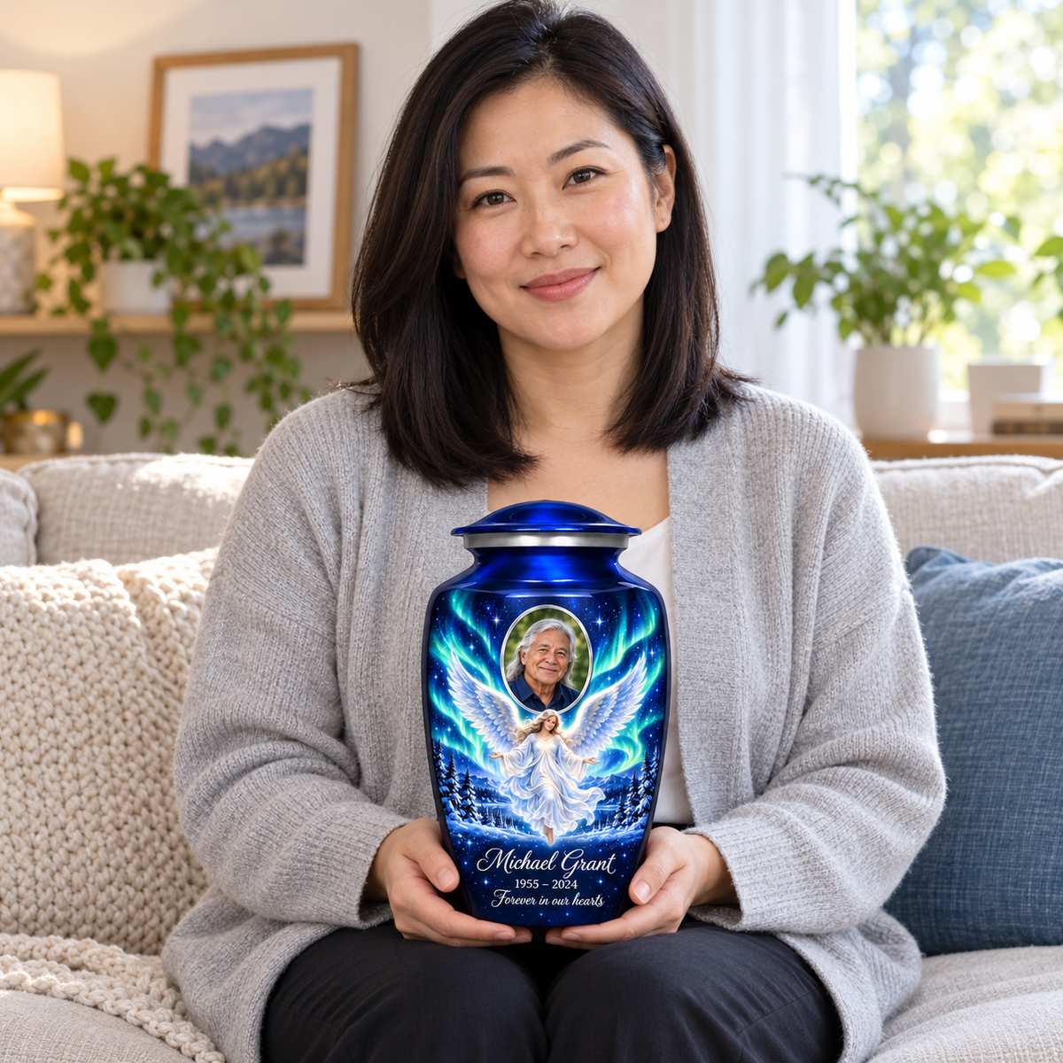 A seated person holding the blue angel urn with a floating angel, aurora sky, snowy trees and an oval sample portrait frame on their lap.