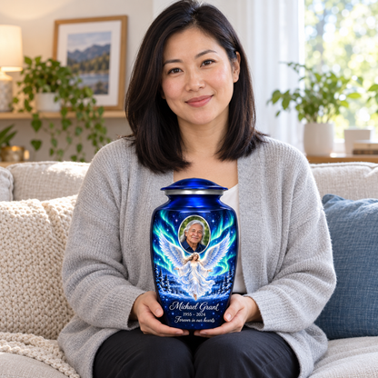 A seated person holding the blue angel urn with a floating angel, aurora sky, snowy trees and an oval sample portrait frame on their lap.