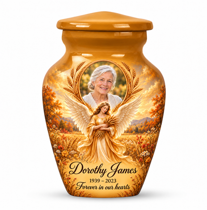 One yellow angel keepsake urn with a wheat bearing angel, autumn meadow and arched sample portrait frame and sample personalization.
