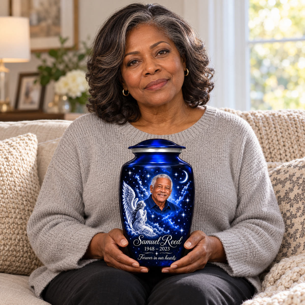 A seated person holding the blue angel urn with a kneeling angel, stars and crescent moon on their lap.