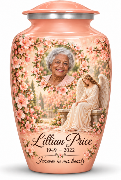 Pink adult urn with a seated angel, peach blossoms and an oval floral sample portrait frame, sample name, dates and tribute.