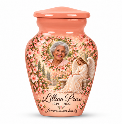 One pink angel keepsake urn with a seated angel, peach blossoms and an oval floral sample portrait frame and sample personalization.