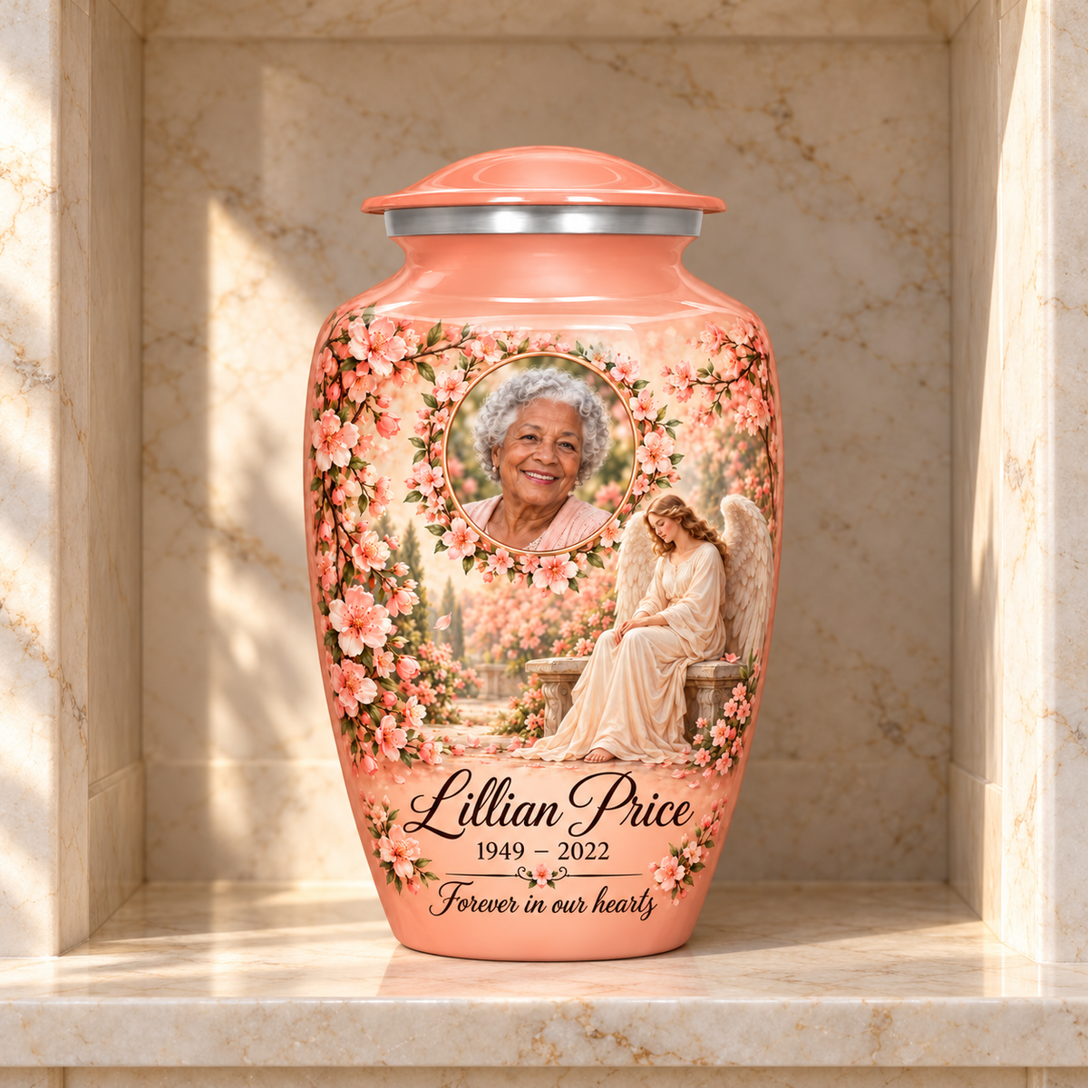 Pink adult urn with a seated angel, peach blossoms and an oval floral sample portrait frame, displayed in a columbarium niche.