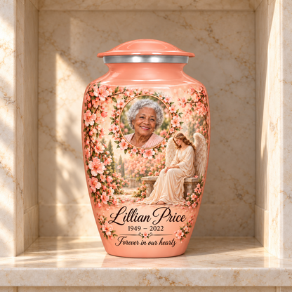 Pink adult urn with a seated angel, peach blossoms and an oval floral sample portrait frame, displayed in a columbarium niche.