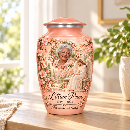 Pink adult urn with a seated angel, peach blossoms and an oval floral sample portrait frame, arranged in a sunlit home.