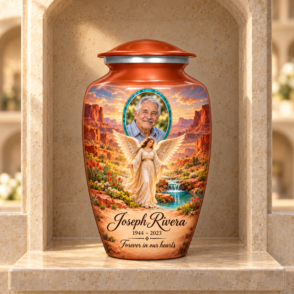 Orange adult urn with an angel beside a desert spring, distant mesas and a turquoise sample portrait frame, displayed in a columbarium niche.