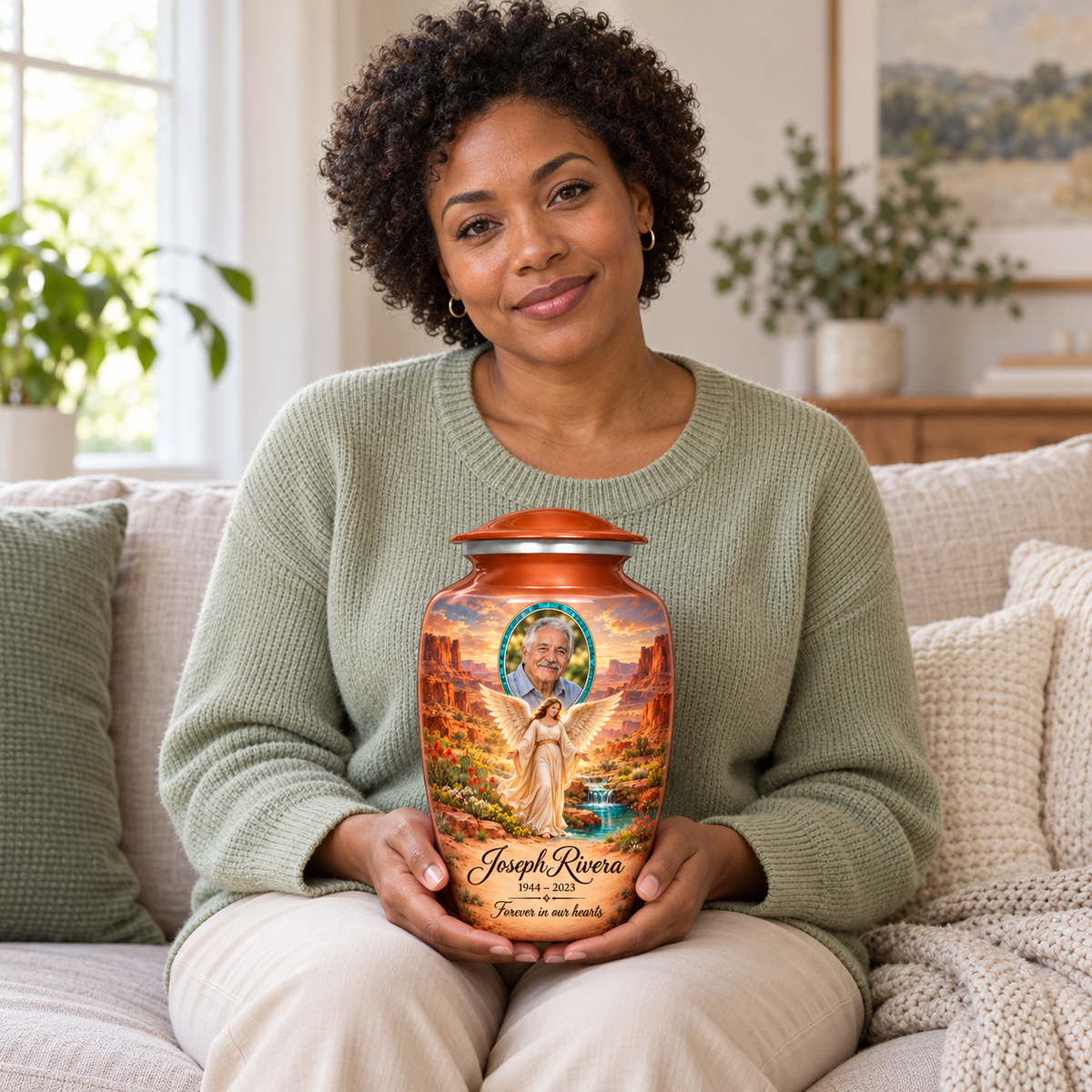 A seated person holding the orange angel urn with an angel beside a desert spring, distant mesas and a turquoise sample portrait frame on their lap.